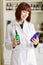 Attractive young lady pharmacist with a lovely smile standing working and holding glass vintage bottles of medicines in