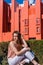 Attractive young lady sitting on a patio in front of  geometric red buildings