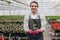 Attractive young man transplanting young plant in greenhouse. Working florist