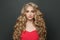 Attractive young woman celebrity with makeup and blonde curly hairstyle in red evening dress on black background