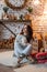 Attractive young woman in a cozy decorated New Year`s room sits on the carpet and hugs a snowman toy