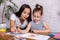 Attractive young woman and her little cute daughter are sitting at the table and having fun while doing homework