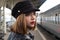 Attractive young woman millenial in black clothes and a hat and glasses at the railway station next to the train