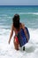 attractive young woman in red bikini walking out to blue sea on sunny beach with body board und