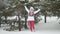 Attractive young woman running in snowdrift shaking snowy branches enjoying the winter in slowmotion during snowfall