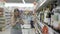 Attractive young woman with shopping cart chooses wine in a bottle store standing in front of shelves full of bottles