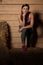 Attractive young woman in sporty dress in a barn posing with hay