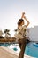 Attractive young woman standing near beautiful pool, lady on vacation, holiday, luxury hotel. Joyful, happy look