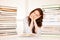 Attractive young woman studies wtih hugr book piles on her desk