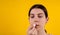 Attractive young woman using hygienic lipstick on yellow background. lips care and protection. woman applying balm on lips