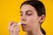 Attractive young woman using hygienic lipstick on yellow background. lips care and protection. woman applying balm on lips