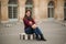 Attractive young womanl in burgundy blouse with a gray scarf sits on a striped dais. Happy woman in Paris