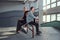 Attractive youth couple with skateboards sitting on a grind rail in skatepark indoors.