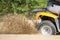 An ATV quadbike get stuck in a sandy road near forest and having wheel-spin making a spray of sand