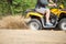 An ATV quadbike get stuck in a sandy road near forest and having wheel-spin making a spray of sand