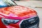 Audi car grille with chrome logo and front hood with reflections of residential buildings. Red car parked on the street