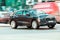 Audi Q8 car driving in city with motion blur, front side view. Brown premium SUV in fast motion on street