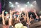 Audience with hands raised at a music festival, blurred stage lights in the background