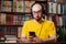 Audiobooks. A bald man with glasses and headphones uses a smartphone. Shelves with books in the background. The concept of fake