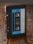 The audiocassette in a classic black case stands edge-on against a brown wooden background. Top view from the side