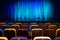 The auditorium in the theater. Blue-green curtain on the stage. Multicolored spectator chairs. Lighting equipment