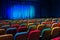 The auditorium in the theater. Blue-green curtain on the stage. Multicolored spectator chairs. Lighting equipment