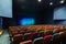 The auditorium in the theater. Blue-green curtain on the stage. Multicolored spectator chairs. Lighting equipment