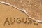 August - word drawn on the sand beach with the soft wave.