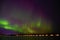 Aurora borealis green beam of northern lights with purple tail beside a lake with reflection in scandenavia