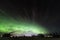 Aurora at clear skies with very tiny clouds shines above a field and lake at Scandinavian countryside, winter time