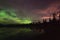 Aurora reflecting of a lake, city lights lighting up clouds - Camera in forground