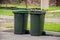 Australian garbage wheelie bins with green lids filled with green garden waste lined up on the street kerbside