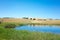 Australian rural landscape of a water pond and farmland on a hill in the distance against the blue sky.