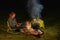 Australian Shepherd dog is lying by the campfire, the kettle with food is cooking and steaming, The woman is reading a
