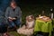 Australian Shepherd dog is lying by the campfire, the kettle with food is cooking and steaming, The woman is reading a