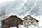 Austrian alpine village scenic landscape with small chalet and wooden barn ,pine forest trees and snow covered mountains on