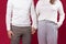 An authentic couple in white sweaters hold hands on a red background. St.Valentine& x27;s Day and human relationship.