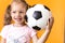 Authentic cute smiling preschool little girl with classic black and white soccer ball look at camera on yellow