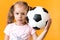 Authentic cute smiling preschool little girl with classic black and white soccer ball look at camera on yellow