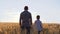 An authentic family. Father and son hold hands and watch the sunset in a wheat field. The concept of a family business