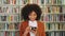 Author and blogger reading reviews online. Young woman browsing and texting on phone with bookshelf in the background