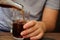 An autistic teenager sitting on a terrace. He is pouring soft drink into a glass with ice cubes.