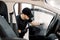 Auto cleaning service and detailing concept. Handsome Caucasian man in black uniform cleaning interior of the car with