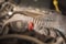 An auto mechanic holds in his hand a torn timing belt with worn out teeth against the background of a car engine