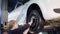 Auto mechanic is twisting manually bolts of a wheels on an automobile, raised by lifting equipment in auto-service