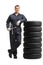 Auto mechanic worker in a uniform leaning on a pile of tires and holding lug wrench tool