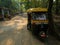 Auto rickshaw standing on a road in a Picturesque lane of a small Indian village in Konkan surrounded by coconut trees