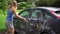 Auto wash. Young attractive blonde woman in shorts washing dirty car on open air