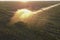 Automatic field watering system. A fountain of water from an irrigation pipe in the field sparkles at morning sunrise