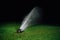 Automatic lawn sprinkler spraying water over golf course green grass